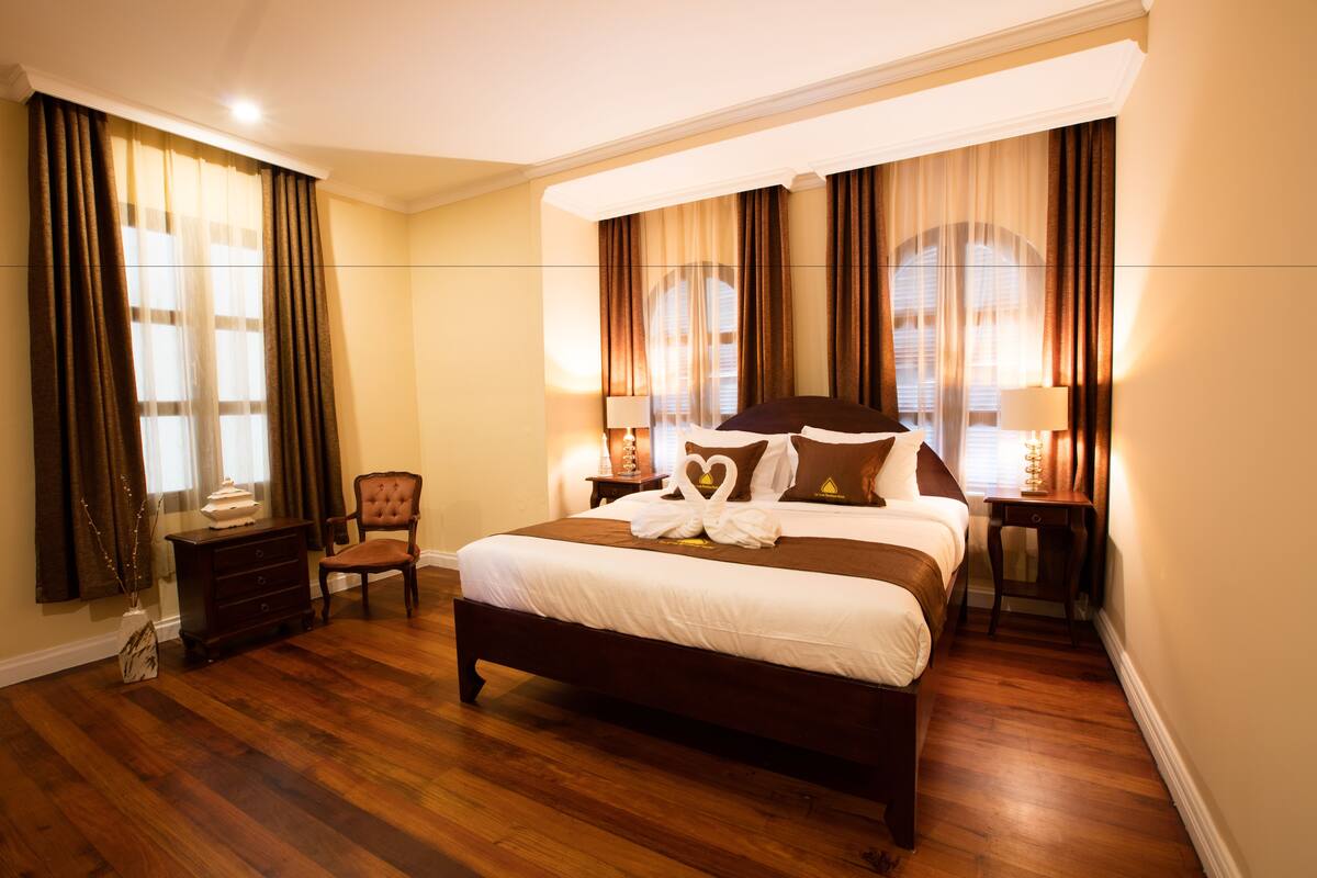 A spacious bedroom with a large bed, a wooden dresser, a chair, and two bedside tables with lamps.