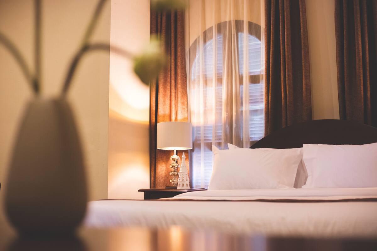 A neatly made bed with white linens, a bedside lamp, and a decorative object on the nightstand.
