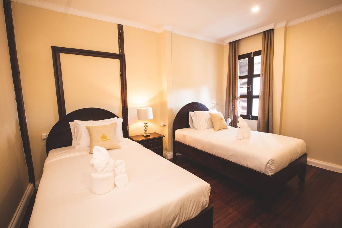 Two single beds with white linens, wooden headboards, and a nightstand with a lamp between them.