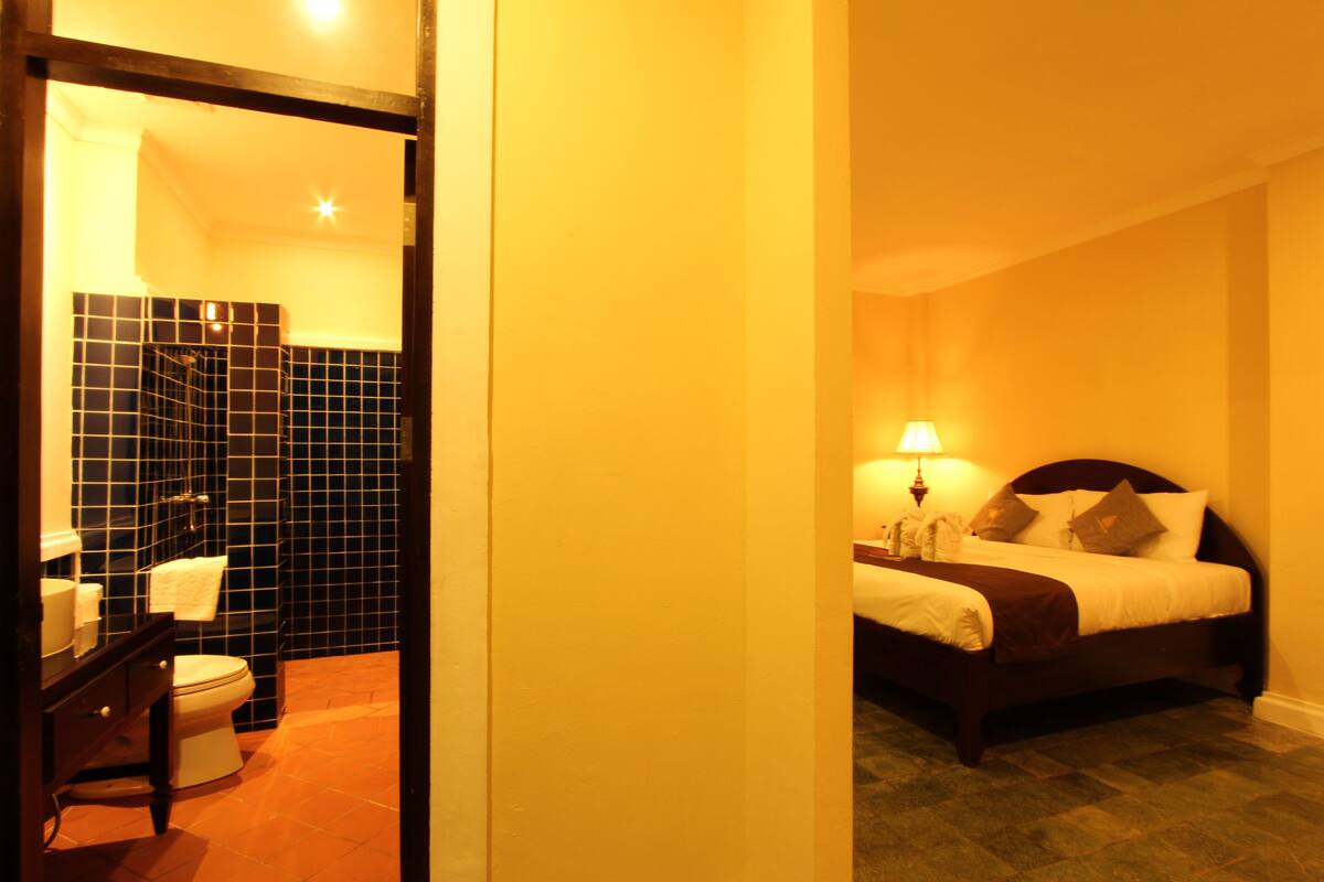 A hotel room with a bed, bedside table, and a bathroom with a toilet and sink.