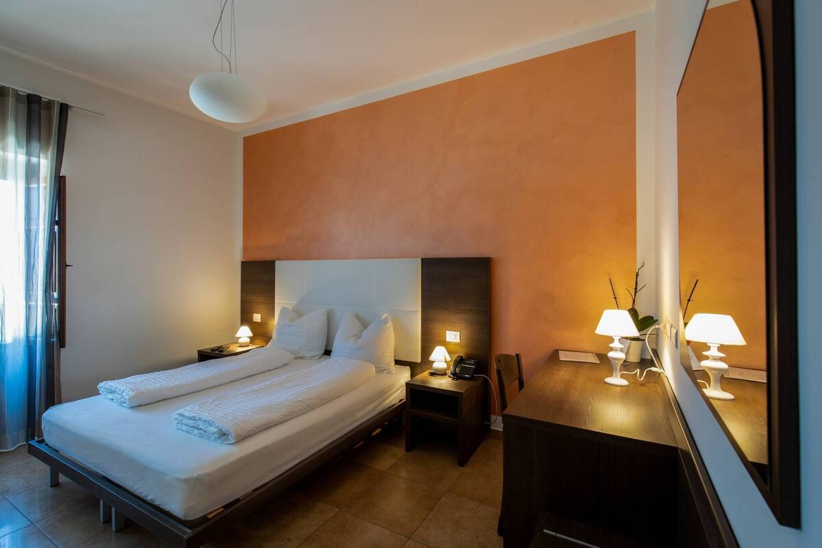 Ein Hotelzimmer mit Bett, Nachttischen, Schreibtisch und Spiegel.