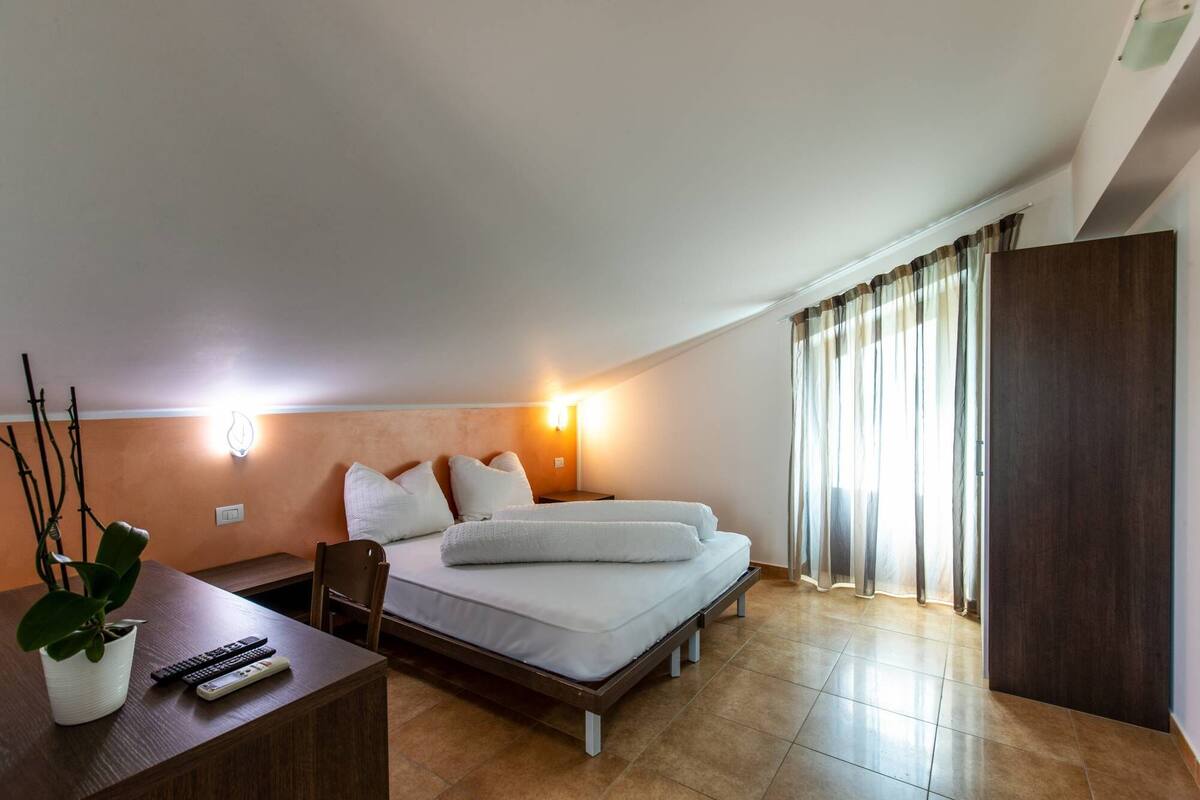 Ein modernes Hotelzimmer mit Bett, Nachttisch und einer Topfpflanze.