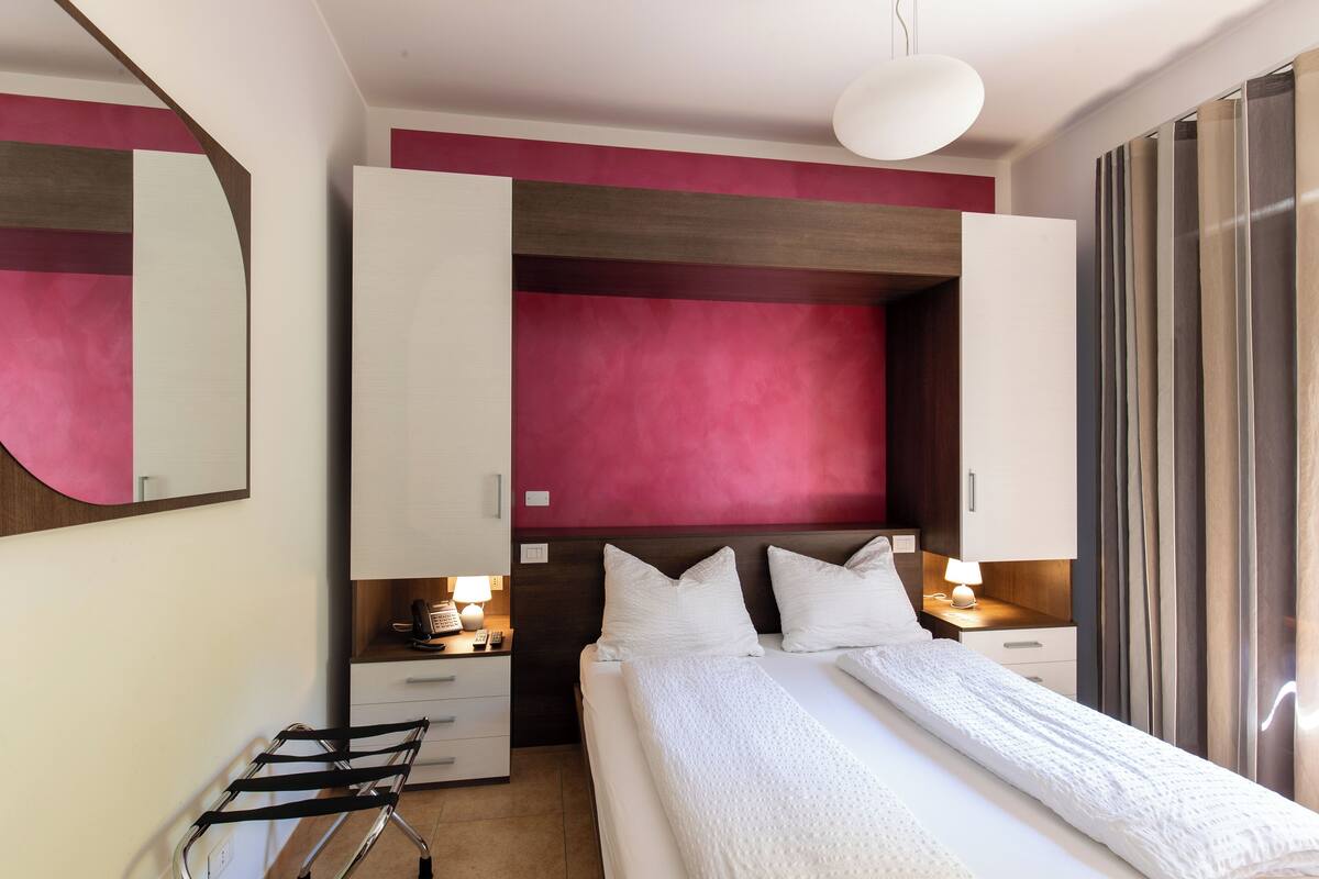 Ein modernes Hotelzimmer mit einem großen Bett, einem Nachttisch mit Lampe, einem Kleiderschrank und einem Spiegel an der Wand.