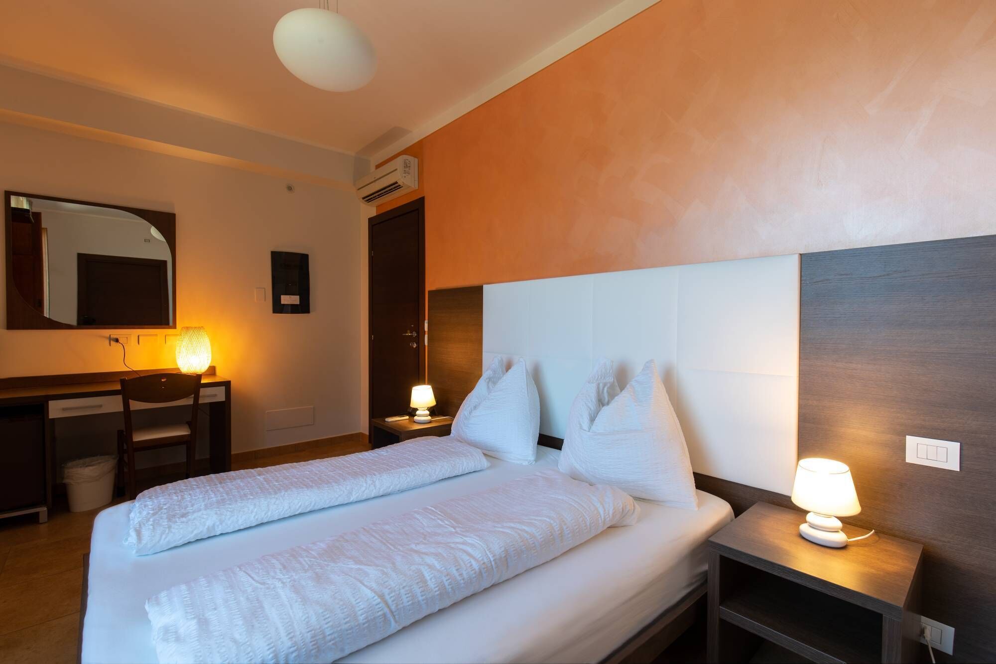 Una habitación de hotel con una cama, lámparas de noche, un escritorio con una silla y un espejo.