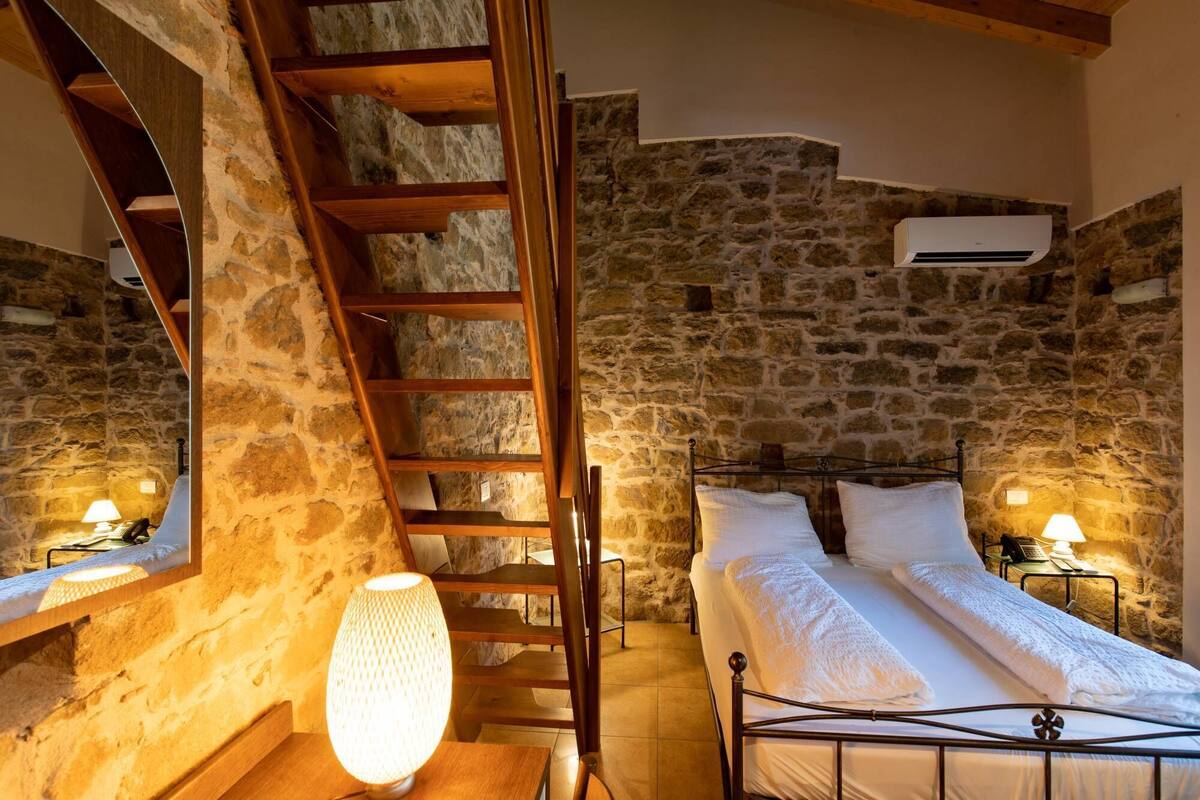 Ein Schlafzimmer mit Steinwand, einer Holzleiter, einem Bett mit weißen Leinen und einer Wand-Klimaanlage.