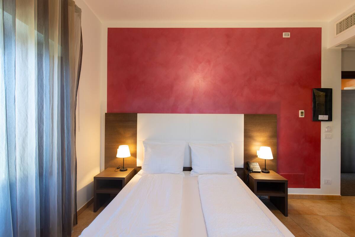 Ein Hotelzimmer mit einem großen Bett, zwei Nachttischen mit Lampen, einer roten Akzentwand und einem Holzkopfstück.