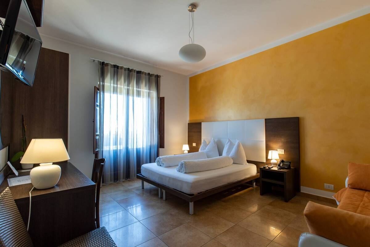 Ein Hotelzimmer mit Bett, Nachttischen, Schreibtisch, Stuhl, Lampe und Fernseher.