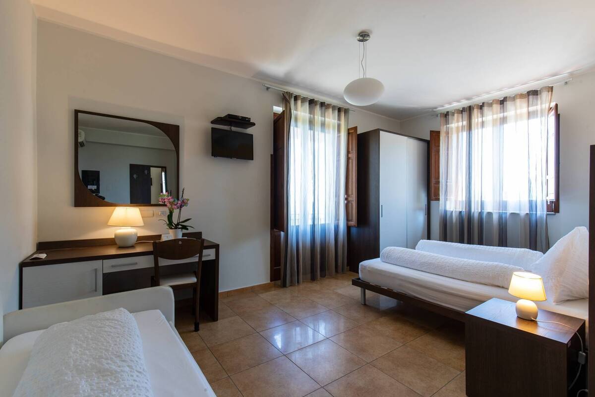 Ein Hotelzimmer mit Bett, Schreibtisch mit Lampe, Stuhl, Spiegel und Fernseher.