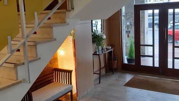 Una escalera conduce a un rellano con un banco, una puerta con la etiqueta 'SALIDA' y una pequeña mesa con plantas.