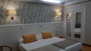 Una cama doble con dos almohadas, una mesita de noche, una silla y un espejo en una habitación de hotel.