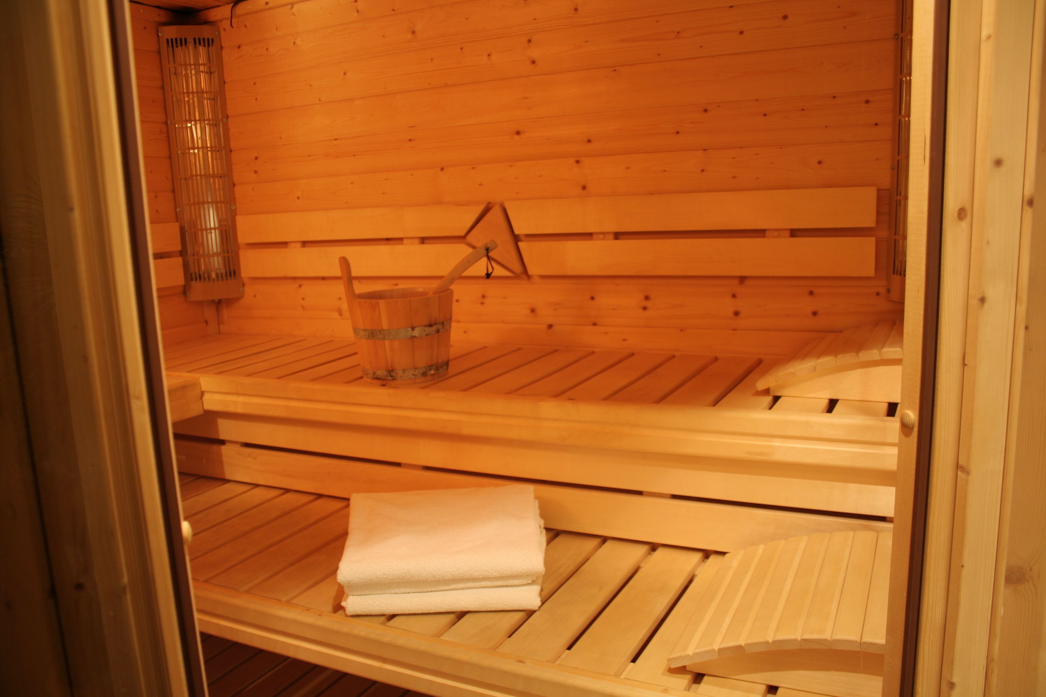 A sauna with wooden benches, a glass container, and a towel.