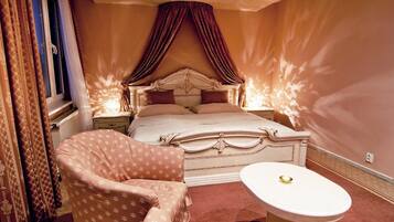 A bedroom with a large bed, a bedside table, a chair, and a window with curtains.
