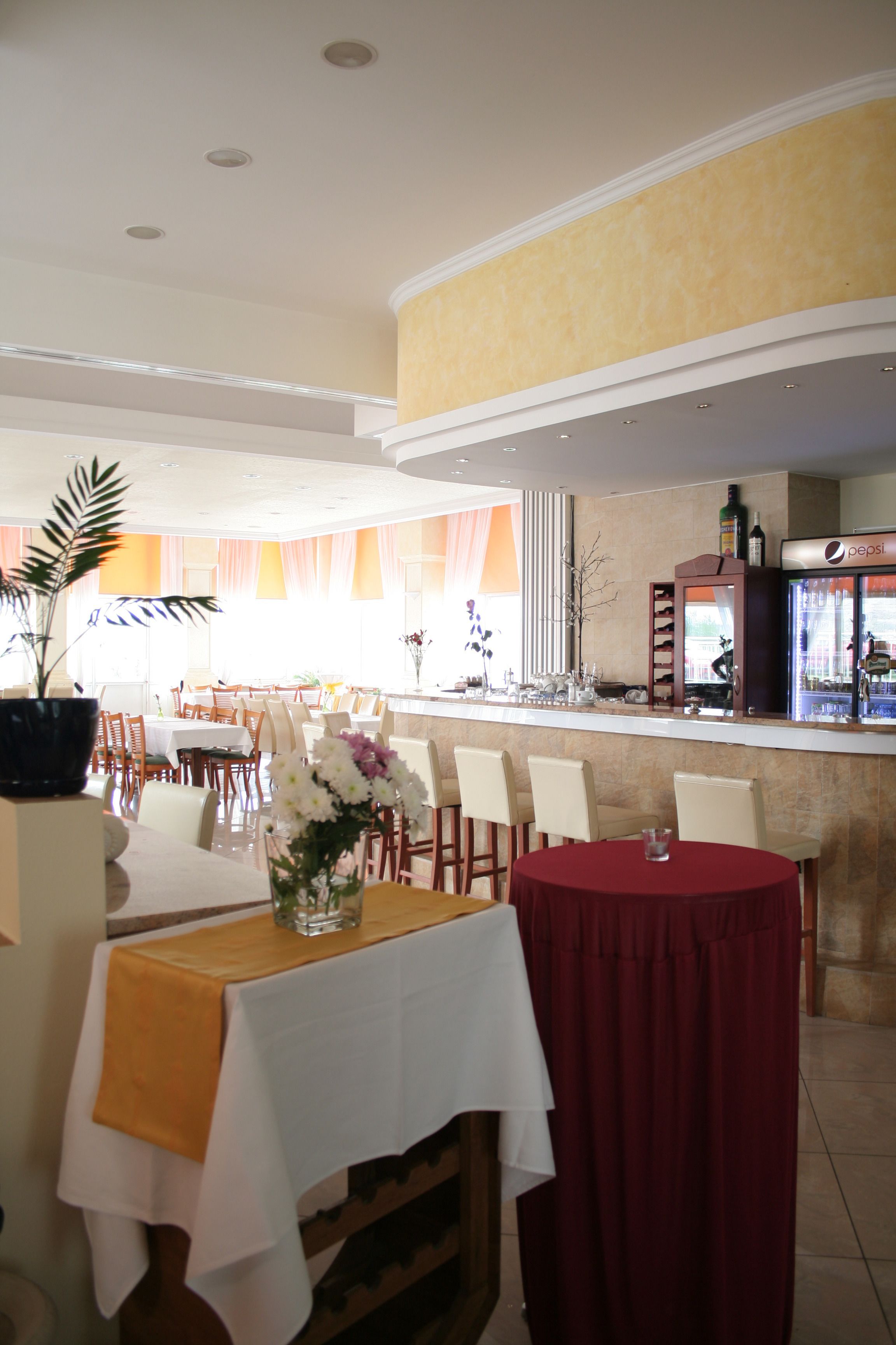 A restaurant with tables and chairs, a bar area, and a refrigerator stocked with beverages.