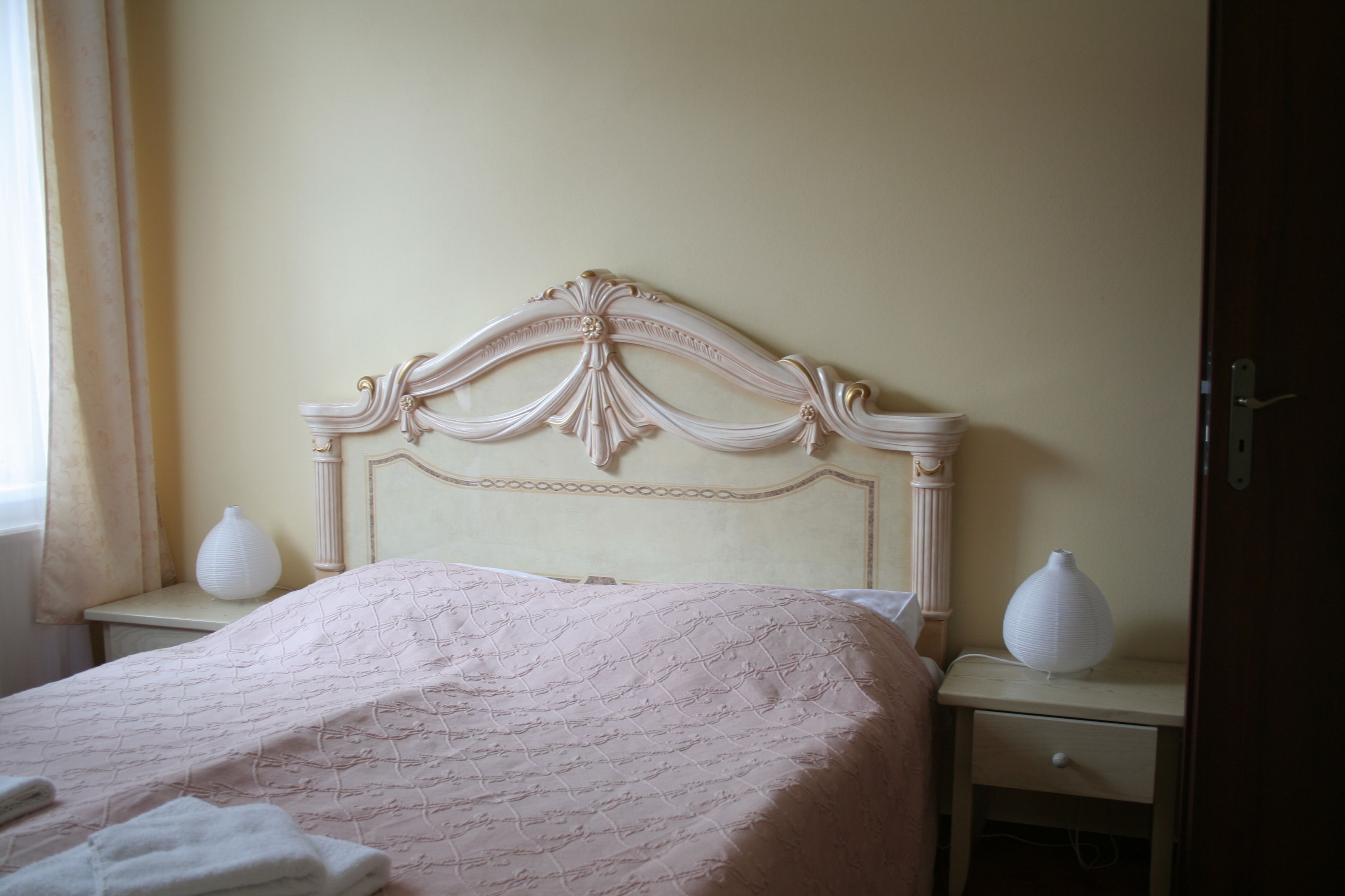 A neatly made bed with a decorative headboard, two bedside tables with white vases, and a window with curtains.