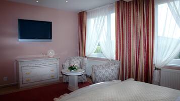 Une chambre d’hôtel comprenant un lit, une commode, une chaise, une petite table avec un vase de fleurs et un téléviseur fixé au mur.