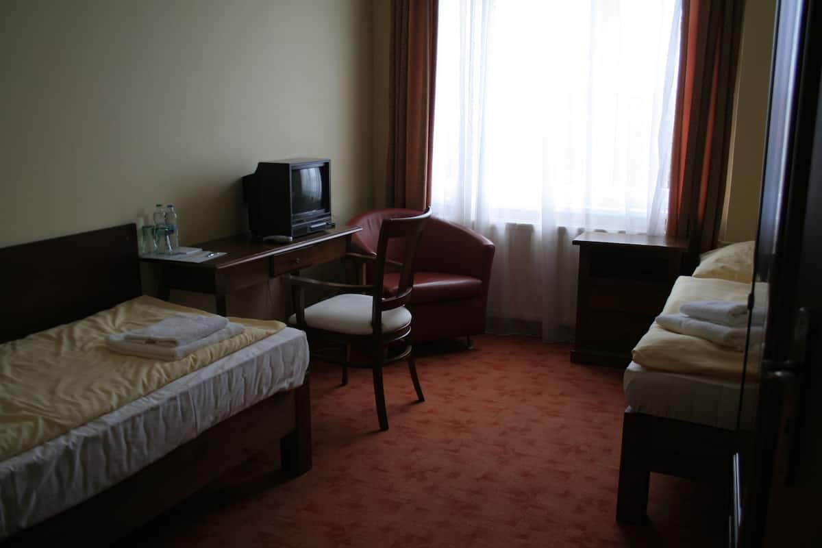 A hotel room with two single beds, a desk with a television, a red chair, and a window with curtains.