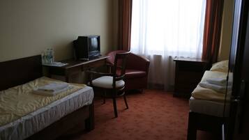 A hotel room with two single beds, a desk with a television, a red chair, and a window with curtains.