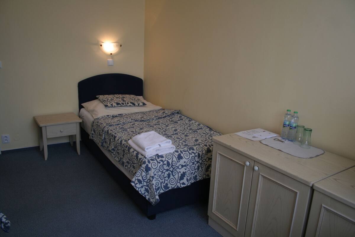 A small, neatly arranged bedroom with a bed, bedside table, and a cabinet with toiletries.