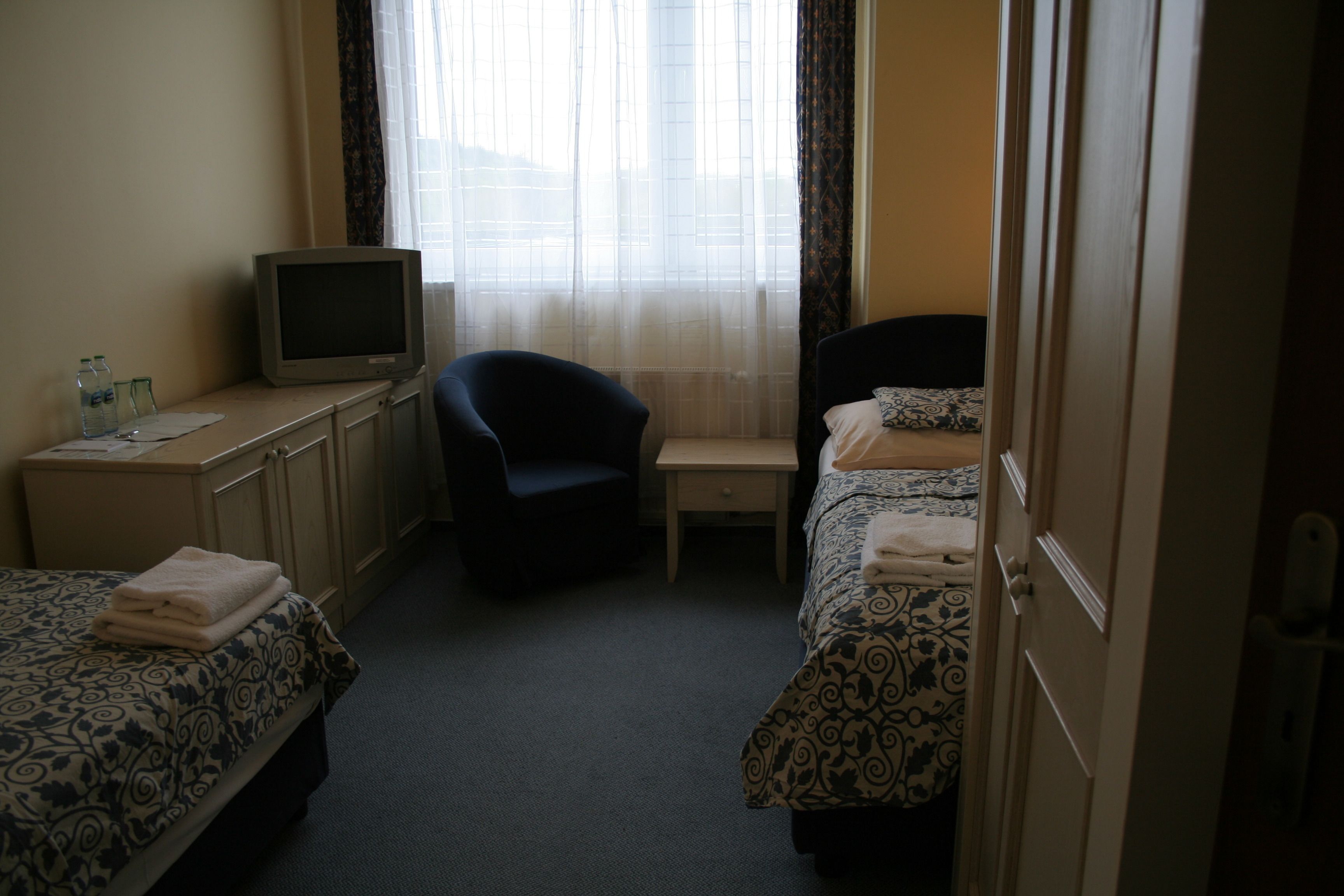Une chambre d’hôtel avec deux lits, un bureau, une chaise, une télévision et une fenêtre avec des rideaux.