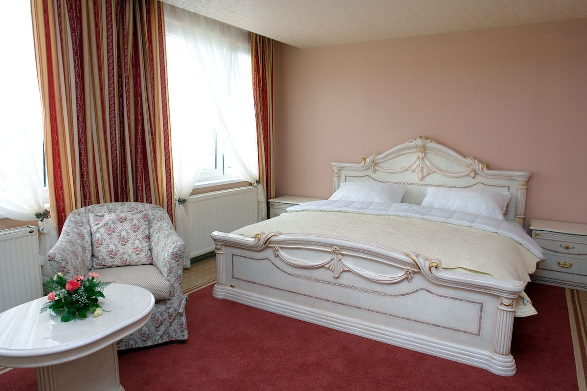 A bedroom with a large bed, a chair, a small table, and a window with curtains.