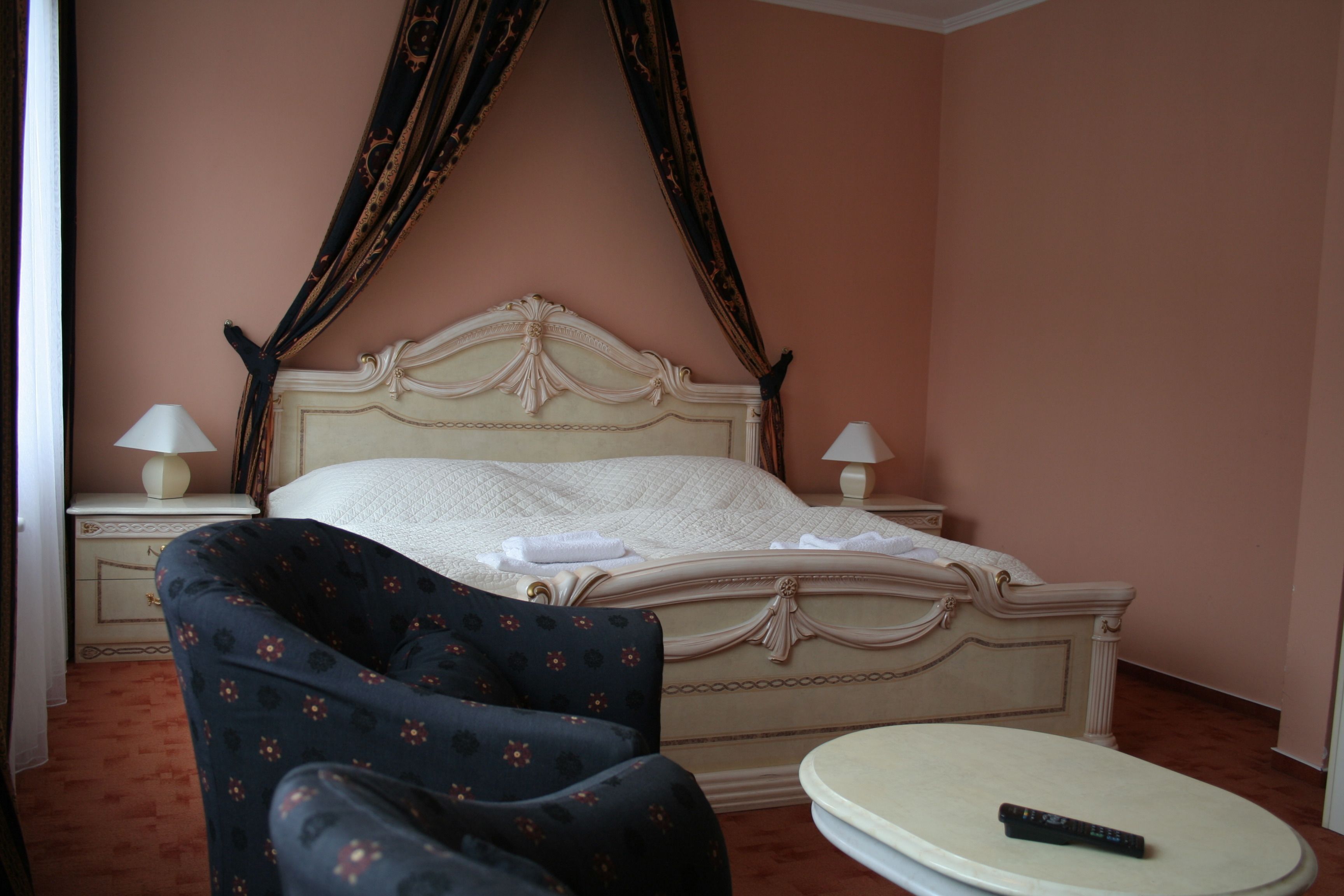 A bedroom with a four-poster bed, two bedside lamps, a round table, and a remote control on the table.