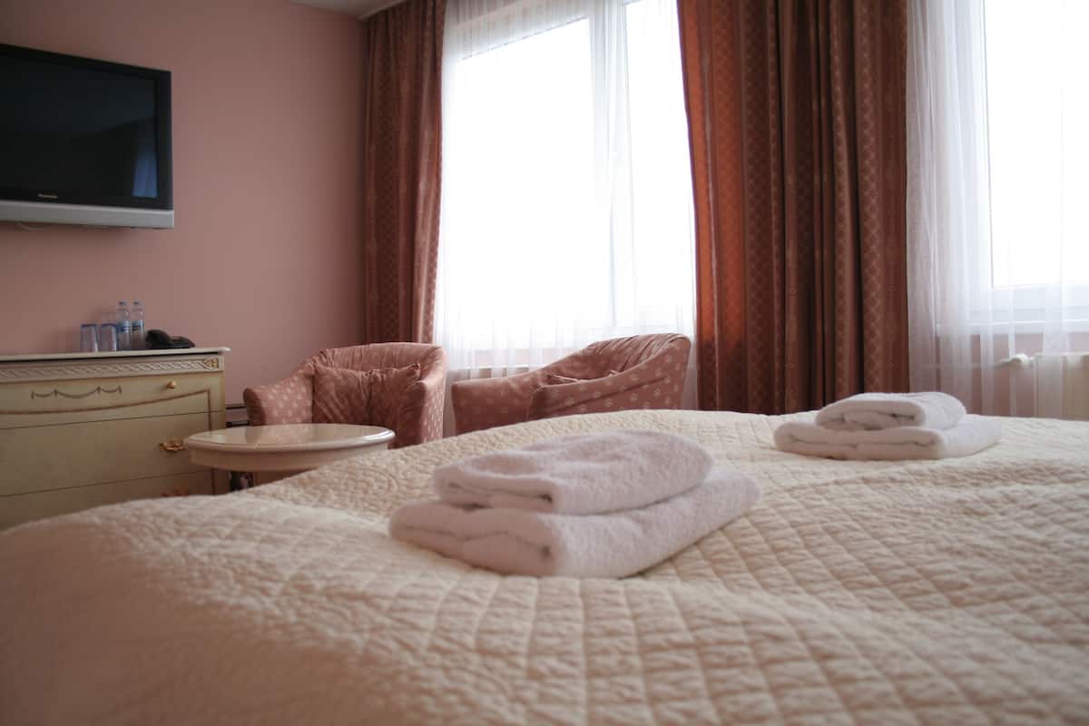 A hotel room with a bed, a bedside table, a chair, a television, and a window with curtains.