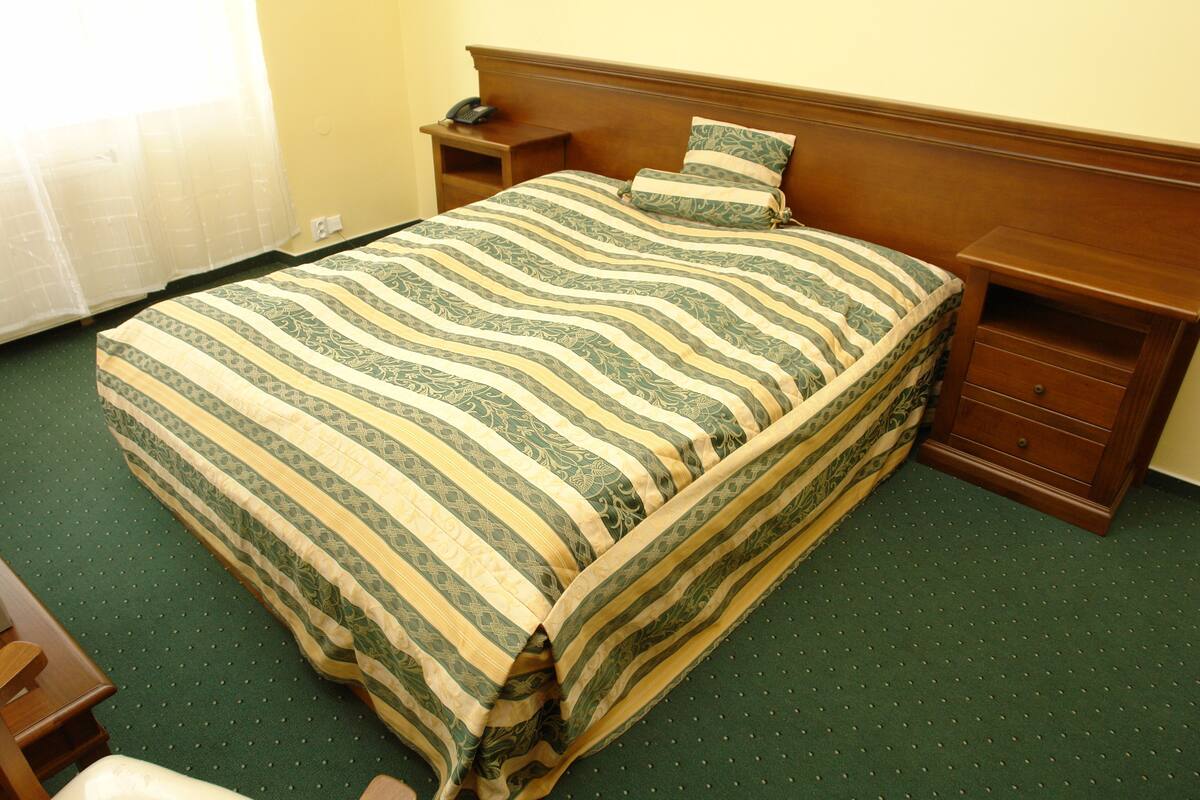 A neatly made bed with a striped bedspread, a bedside table with a telephone, and a nightstand with a lamp.