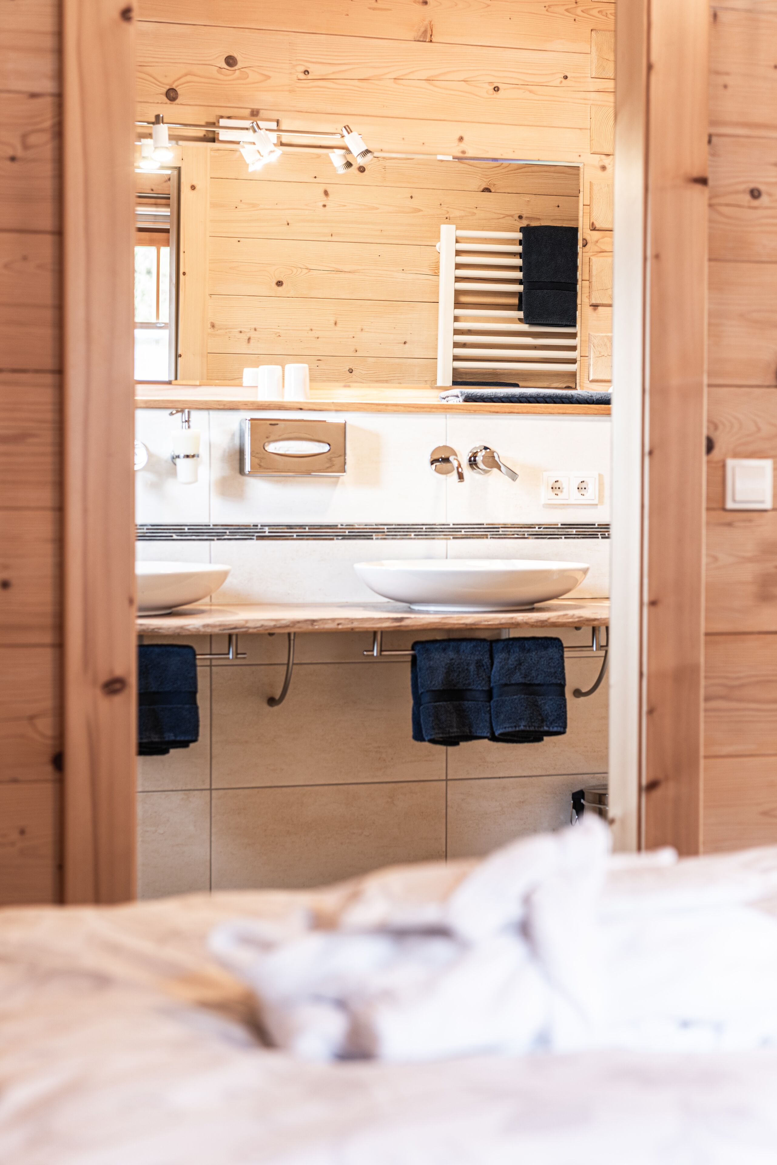 Ein Badezimmer aus Holz mit einem großen Spiegel, zwei Waschbecken und Handtüchern, die an Haken hängen.