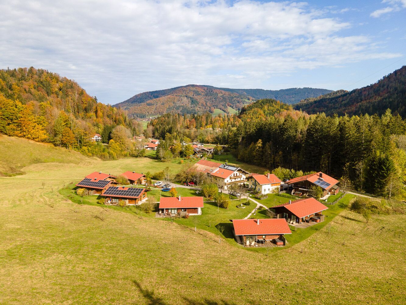 A cluster of houses with red roofs, surrounded by green fields and forested hills.
