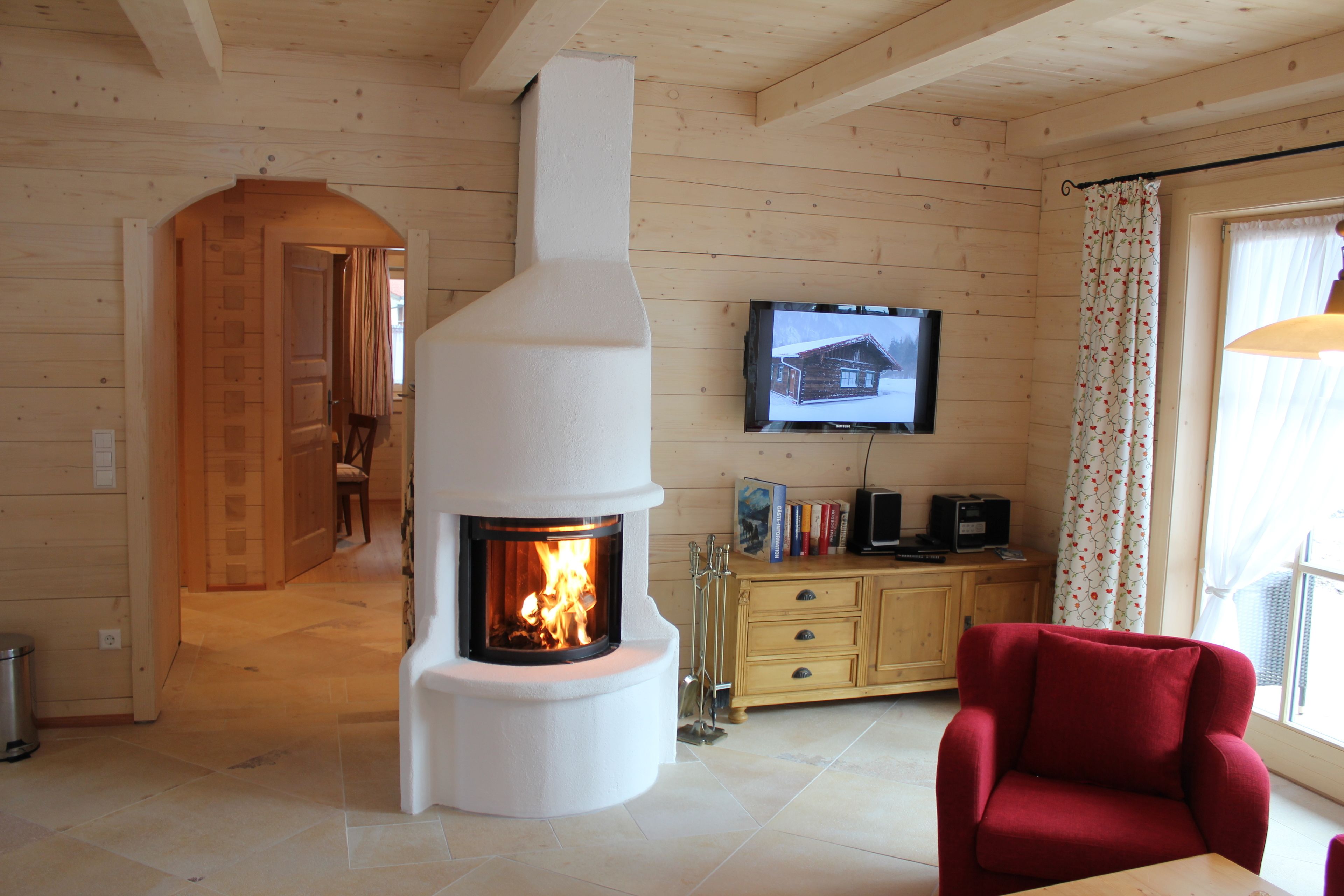 A cozy living room with a fireplace, wooden walls, a television, and a red armchair.