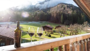 A wooden balcony with a bottle of wine and two glasses on it, overlooking a mountainous landscape with a river and houses. - Chalets&Apartments beim Waicher (Ruhpolding)