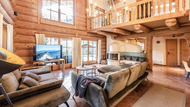 A spacious log cabin interior with a large living area, a fireplace, and a balcony with a wooden railing. - Chalets&Apartments beim Waicher (Ruhpolding)