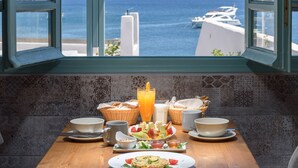A table with breakfast items and a view of the sea through a window. - Sublime Villa & Caves (Santorini)