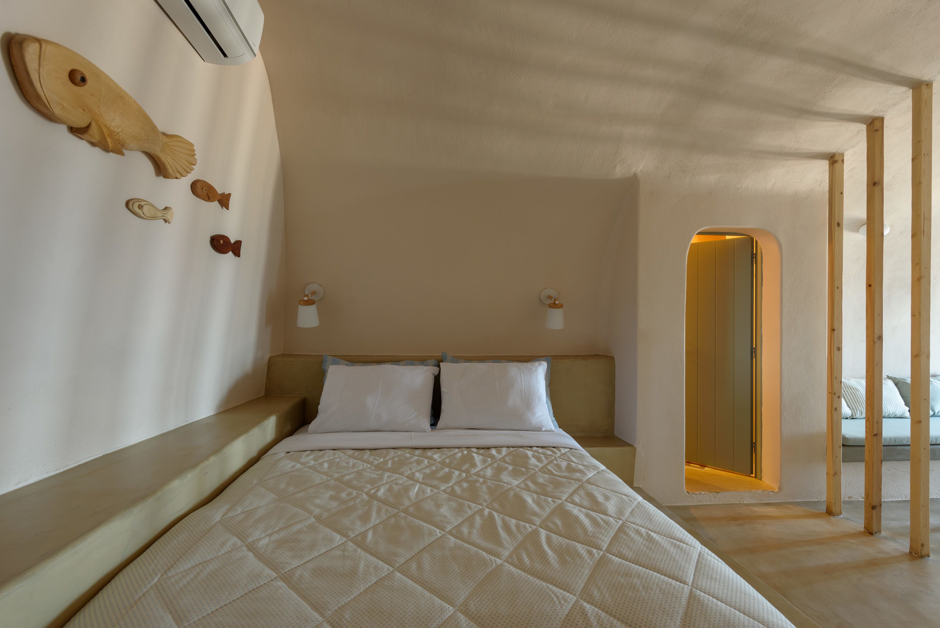 Une chambre à coucher avec un lit, une tête de lit en bois, une décoration murale représentant des poissons et une porte donnant sur une autre pièce.