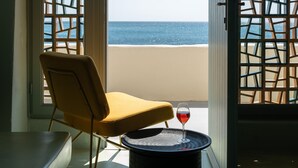 A room with a view of the beach, a chair, and a table with a glass of red wine. - Sublime Villa & Caves (Santorini)