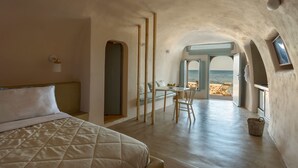 A bedroom with a bed, a desk, and a view of the sea. - Sublime Villa & Caves (Santorini)