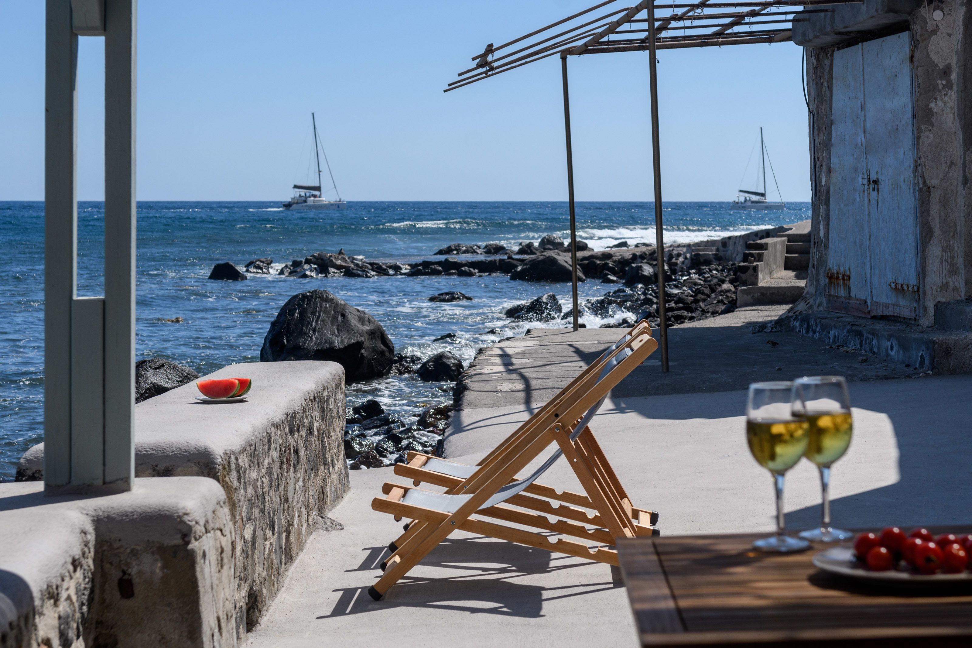 Eine Terrasse am Strand mit einem Tisch, zwei Gläsern Weißwein und einer Tomatenschale.