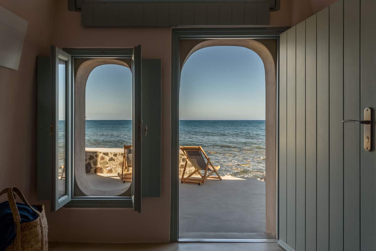A room with a view of the sea through an open door, a beach chair, and a stone wall.