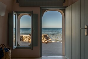 Una habitación con vistas al mar a través de una puerta abierta, una silla de playa y una pared de piedra.
