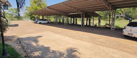 Un área de estacionamiento techada con pavimento de concreto, palmeras y una torre de servicios al fondo.