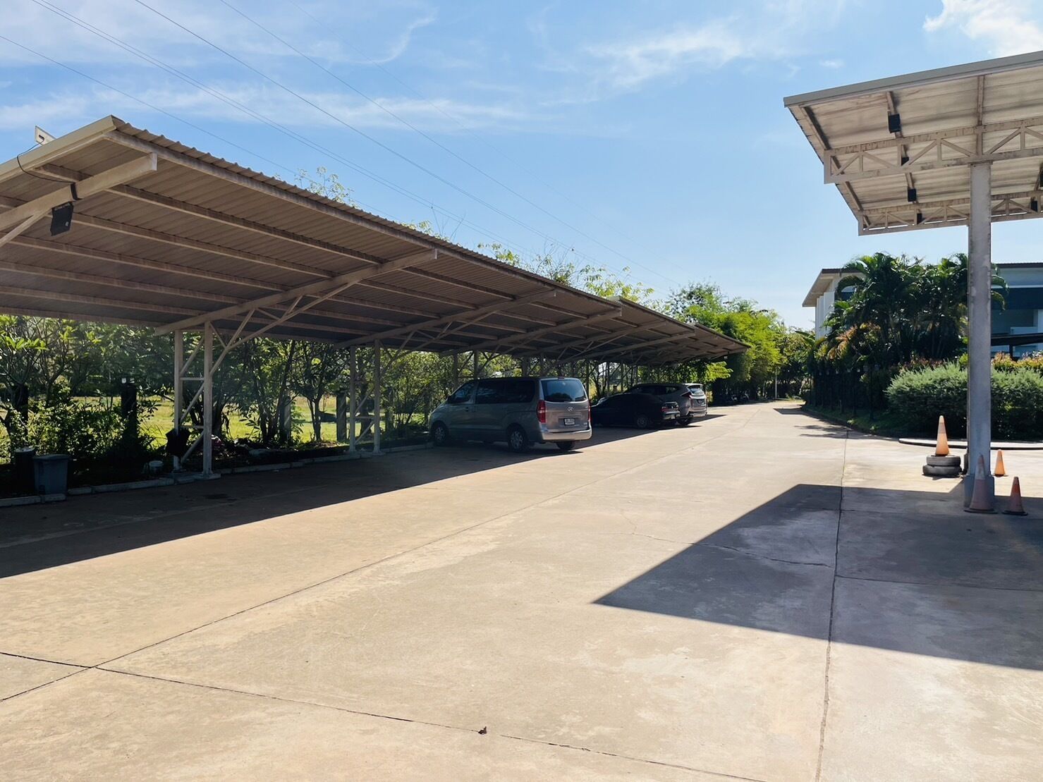 Un área de estacionamiento techada con vehículos, piso de concreto y un edificio al fondo.