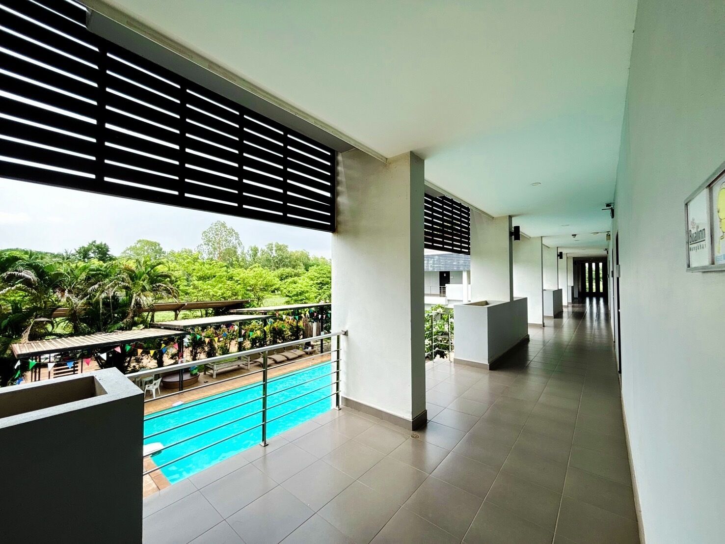 A modern hotel corridor with a pool area, outdoor seating, and a view of greenery.
