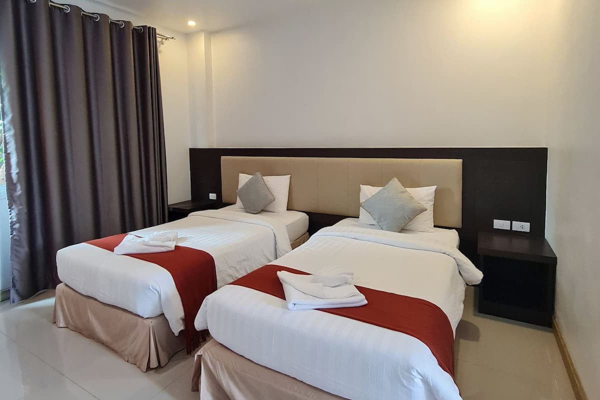 Une chambre d’hôtel avec deux lits, une tête de lit, une table de chevet et une fenêtre avec des rideaux.