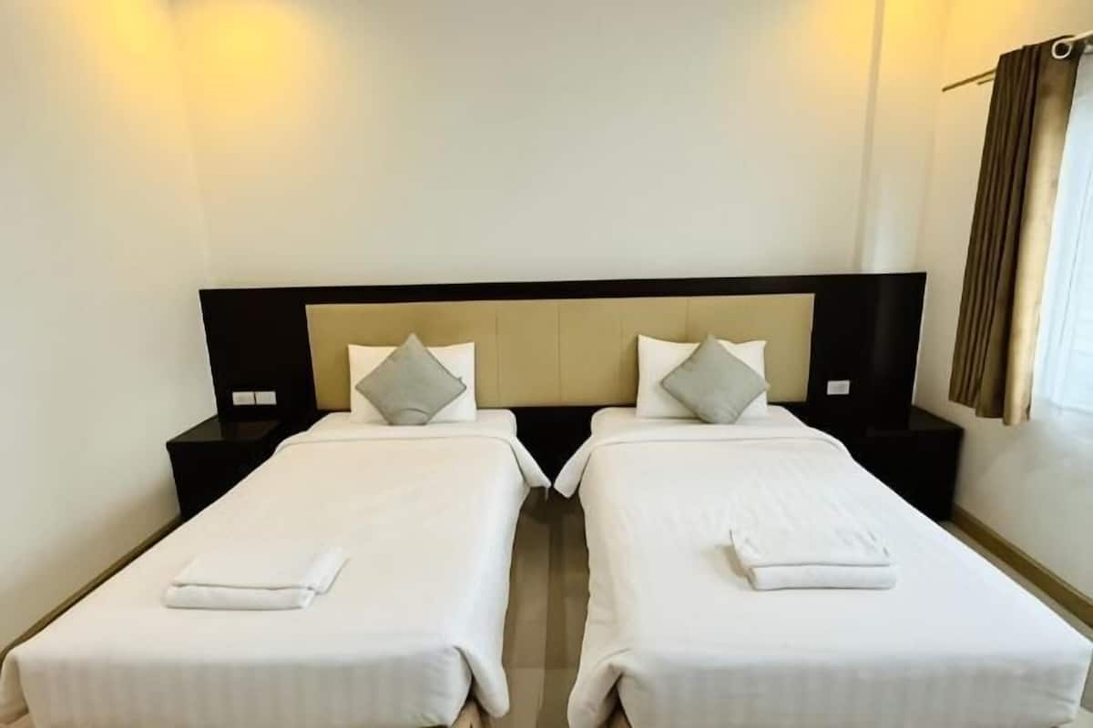 Une chambre d’hôtel avec deux lits simples, chacun équipé d’un oreiller et d’une couverture, ainsi qu’une table de chevet et un téléviseur fixé au mur.