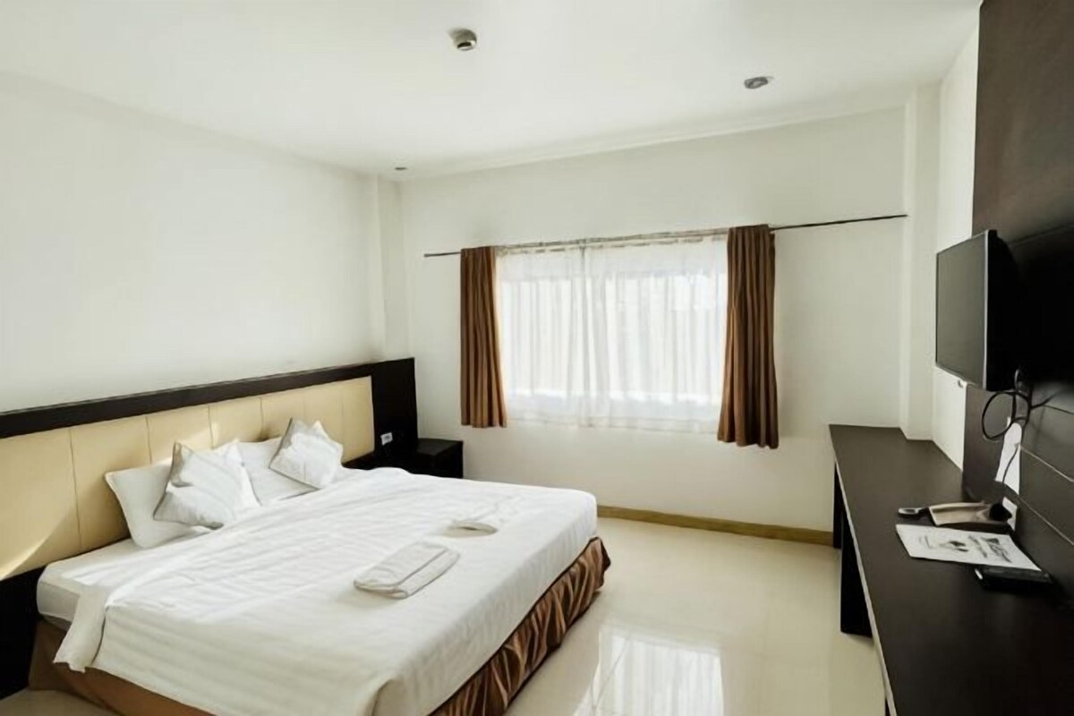 A hotel room with a bed, a desk, a television, and a window with curtains.
