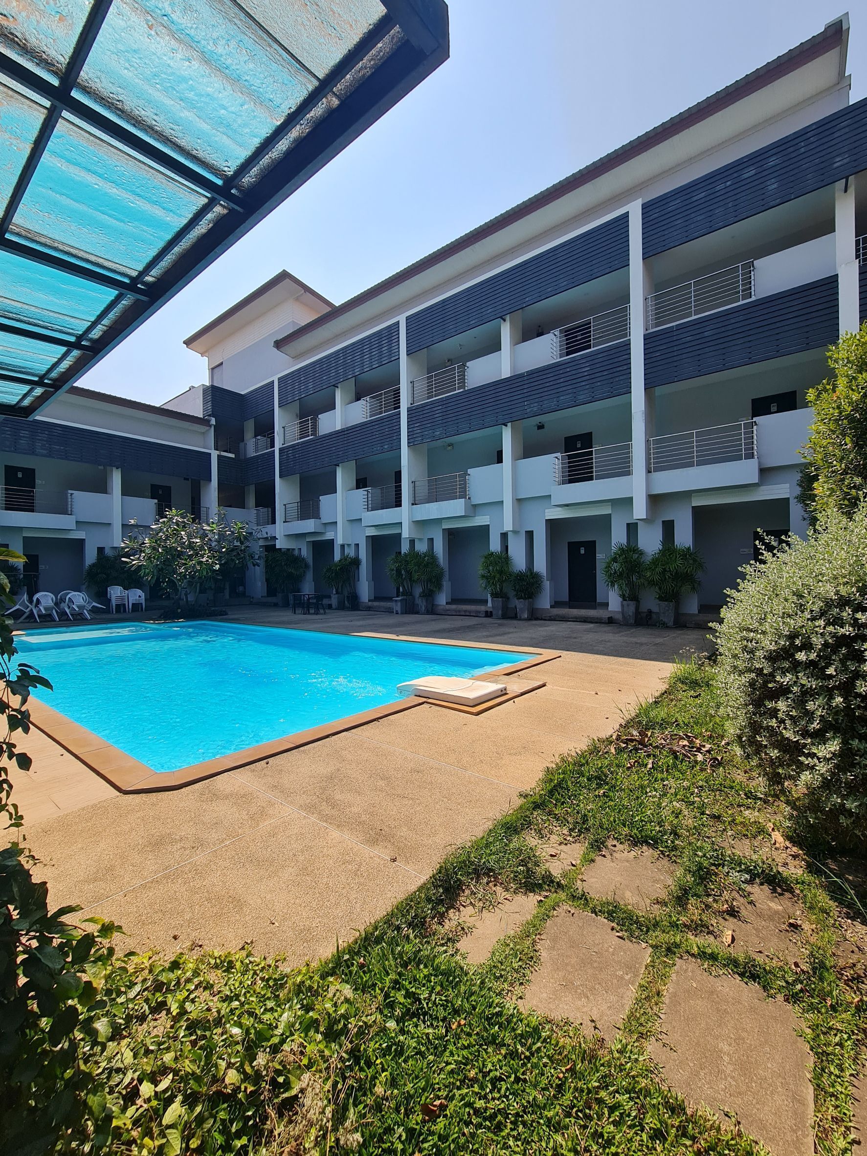 A modern building with a swimming pool, multiple balconies, and potted plants.