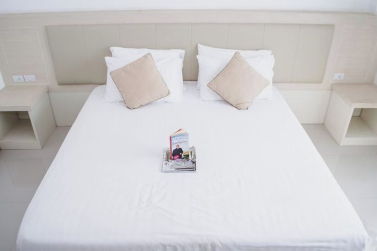 Una cama bien hecha con una revista, dos almohadas y un cabecero.