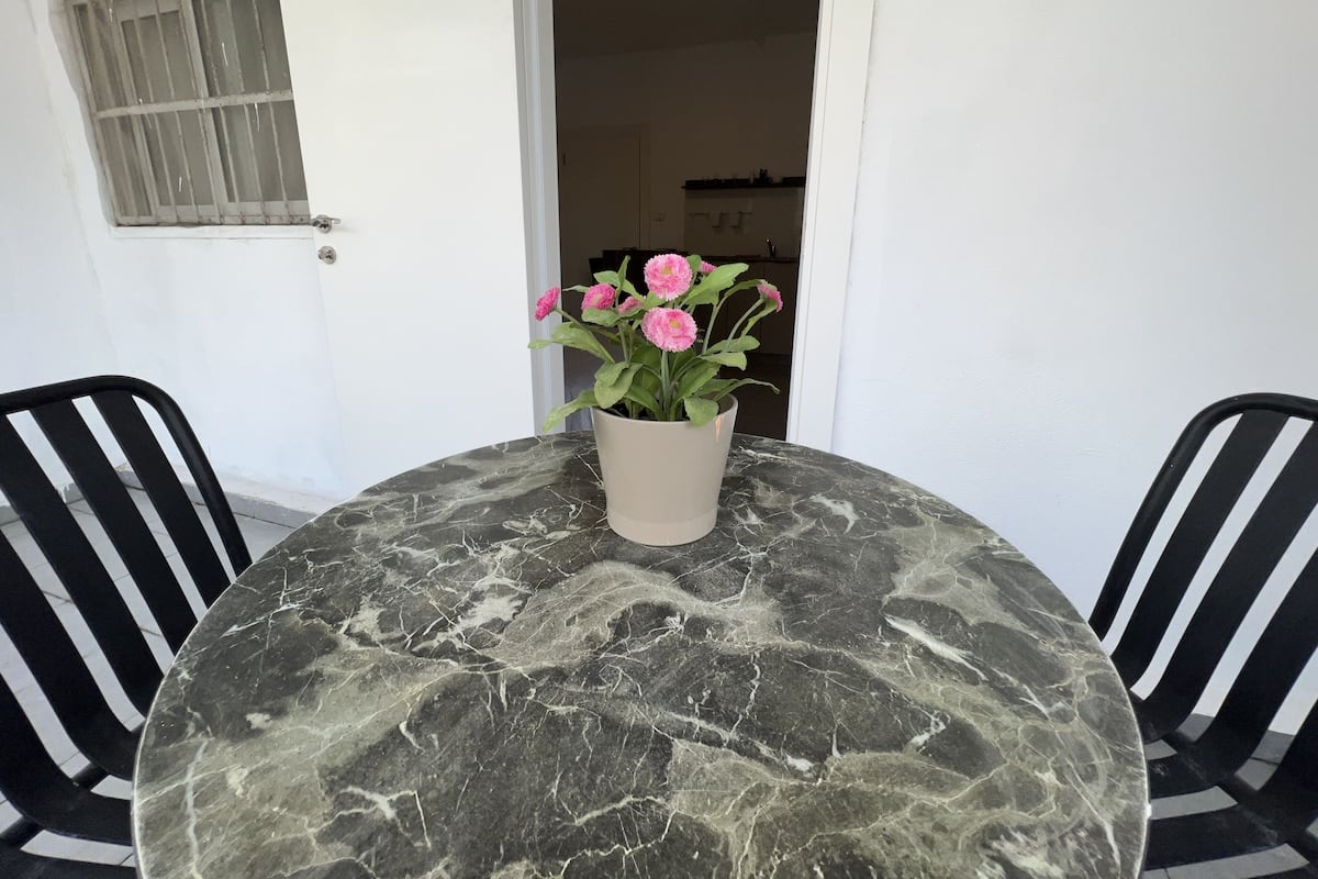 A round table with a marble top, two black chairs, and a potted plant with pink flowers.