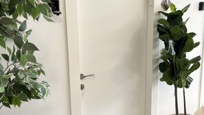 Une porte blanche avec un trou de serrure et une poignée, un pot de fleurs sur la droite et une petite plante sur la gauche.