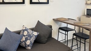 Un salon moderne comprenant un canapé, deux œuvres d’art encadrées, une petite table à manger et un téléviseur.